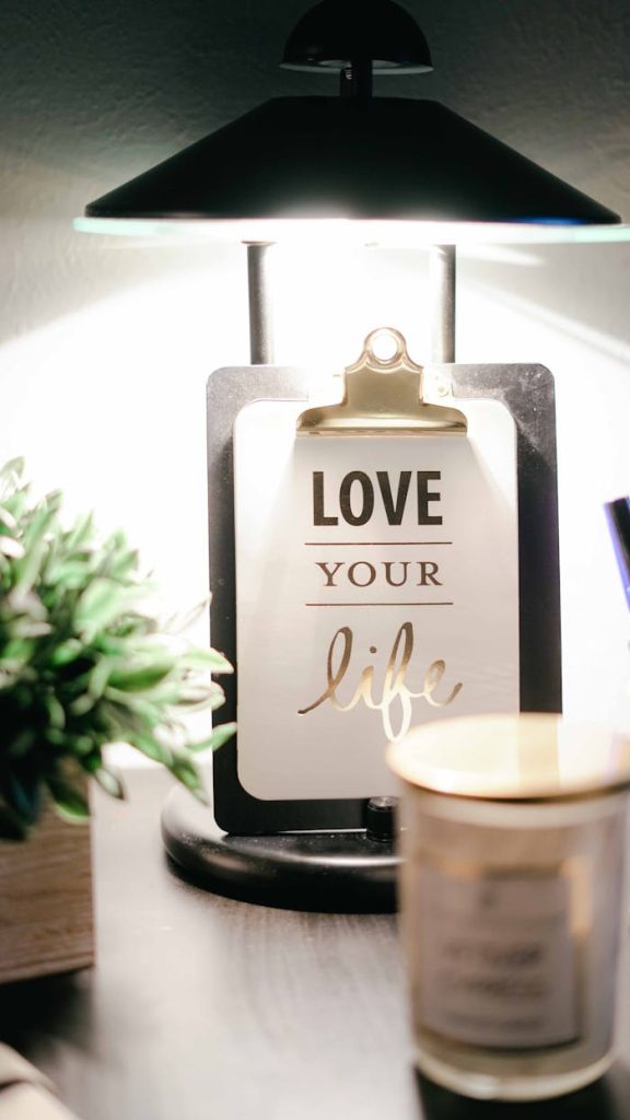 love-your-life-clipboard-decor-811575 A warmly lit desk setup featuring a lamp, inspirational clipboard, and decor for a cozy ambiance.